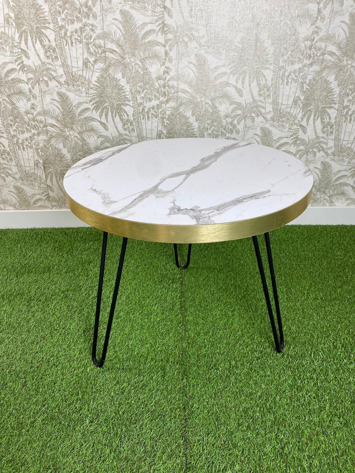 Una mesa redonda con tapa de mármol y patas de horquilla reposa sobre una alfombra verde.