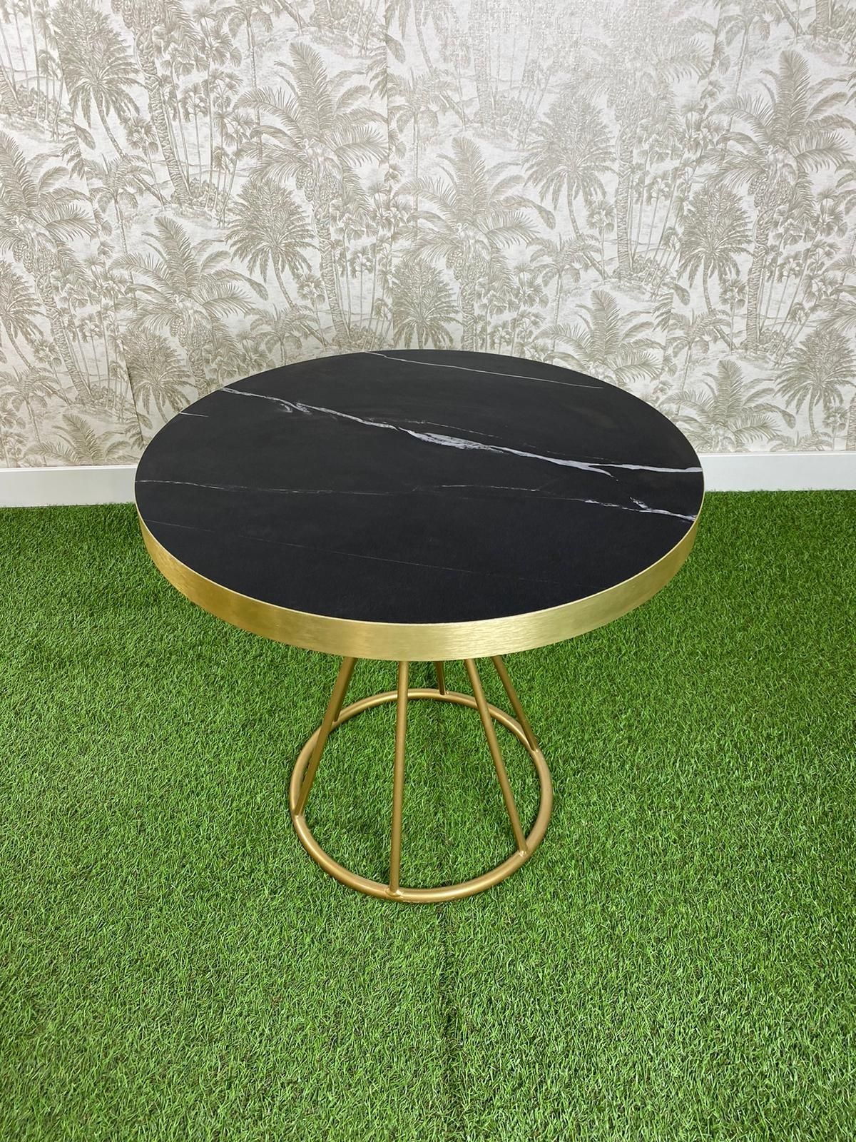 Una mesa de mármol negro con un marco dorado reposa sobre una alfombra verde.