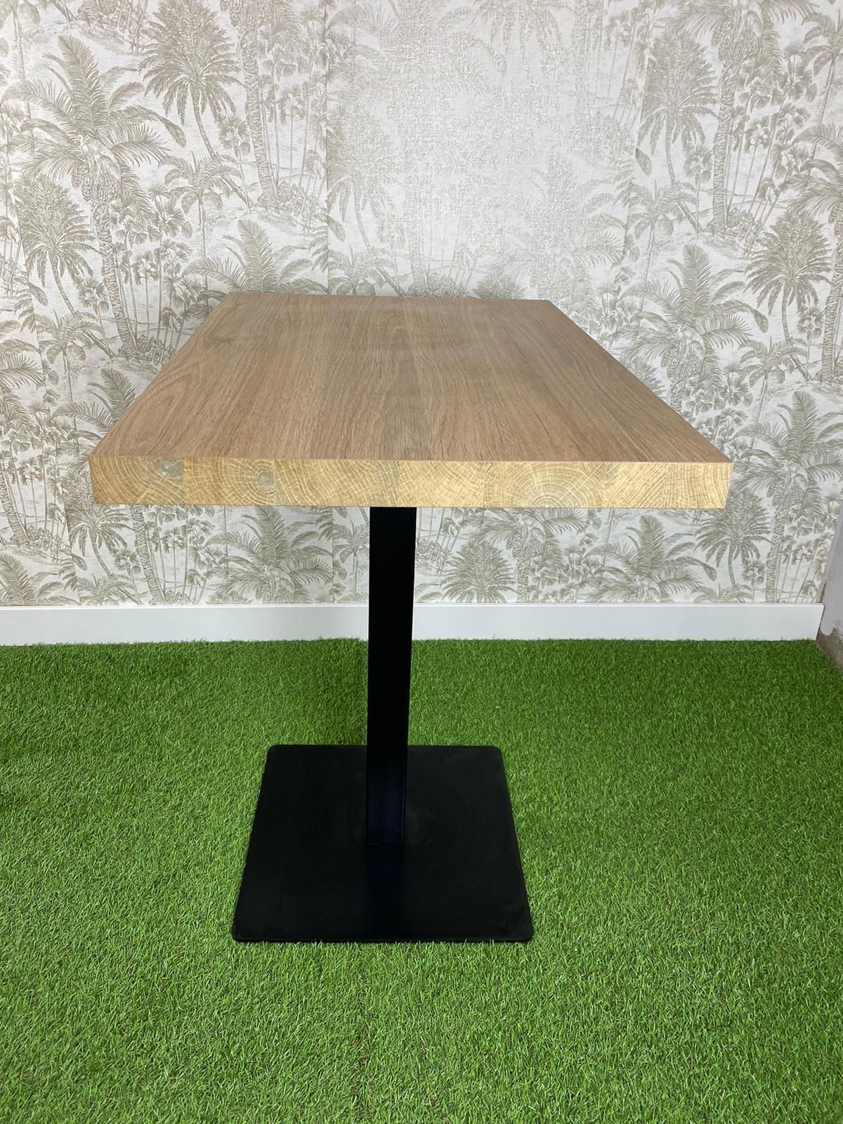 Una mesa de madera con una base negra está colocada encima de una alfombra verde.