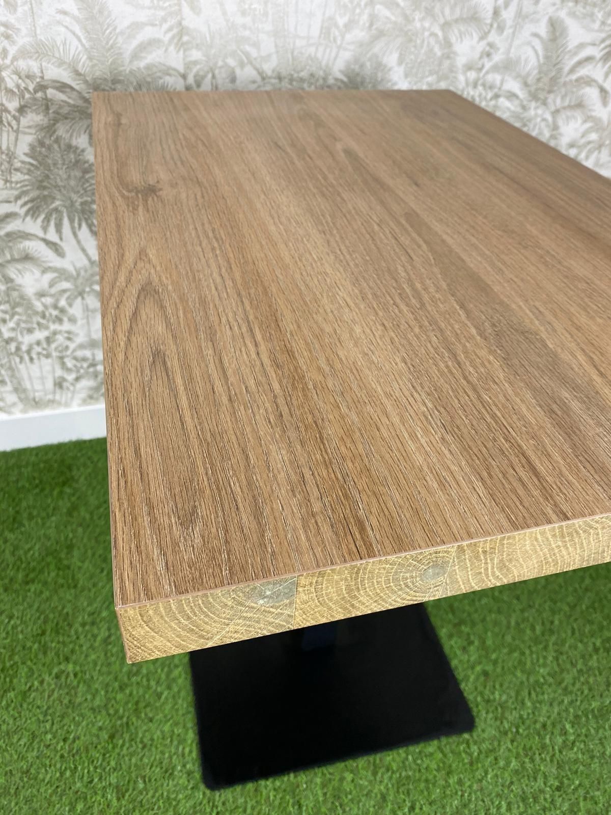 Una mesa de madera con una base negra está colocada encima de una alfombra verde.