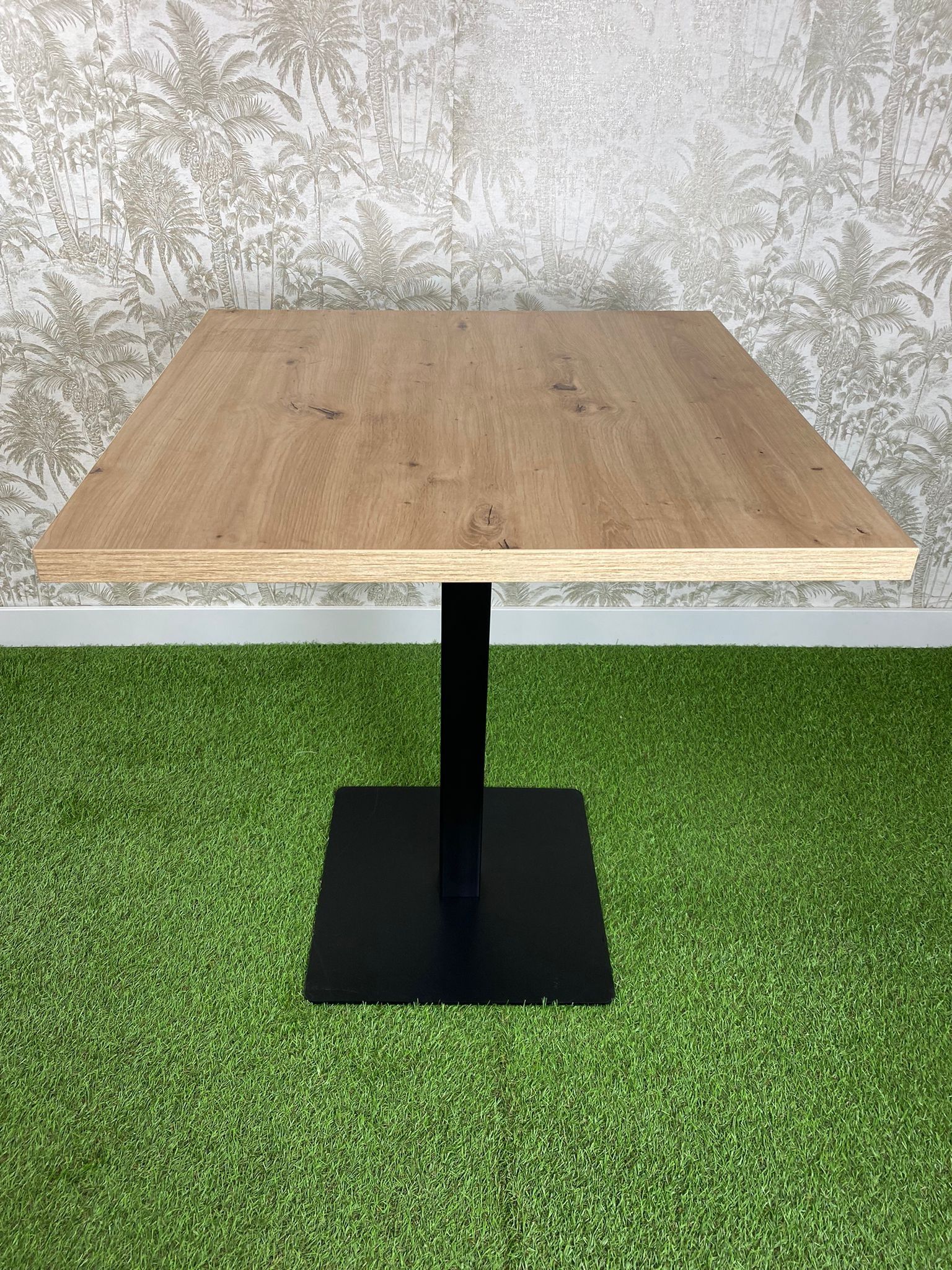 Una mesa de madera con una base negra está colocada encima de una alfombra verde.