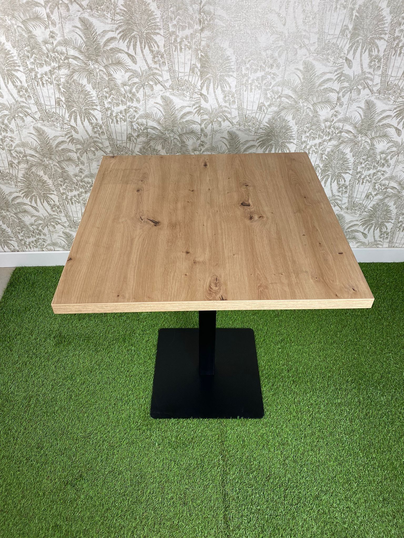 Una mesa de madera con una base negra está colocada encima de una alfombra verde.