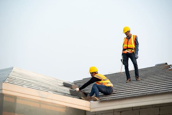 Dos trabajadores de la construcción con cascos y chalecos de seguridad instalando tejas en un edificio.