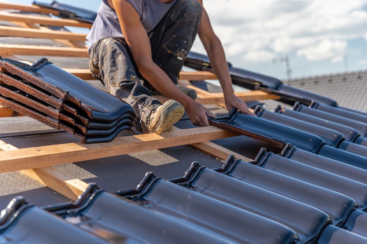 Techador instalando tejas cerámicas de color gris oscuro sobre una estructura de madera, en un entorno exterior.