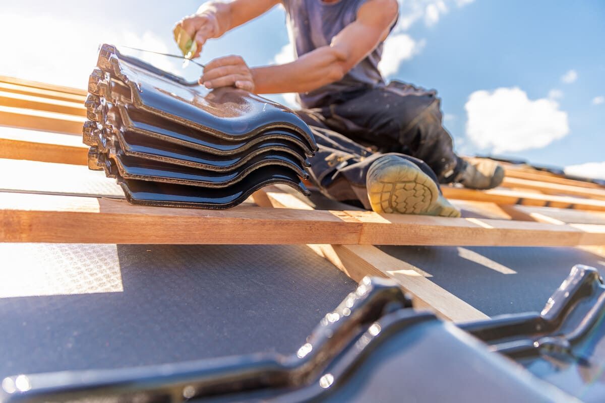 Techador instalando tejas oscuras en una estructura de techo de madera bajo un cielo azul.