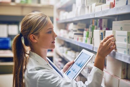 Farmacista in camice bianco controlla le scatole dei medicinali su uno scaffale della farmacia con un tablet