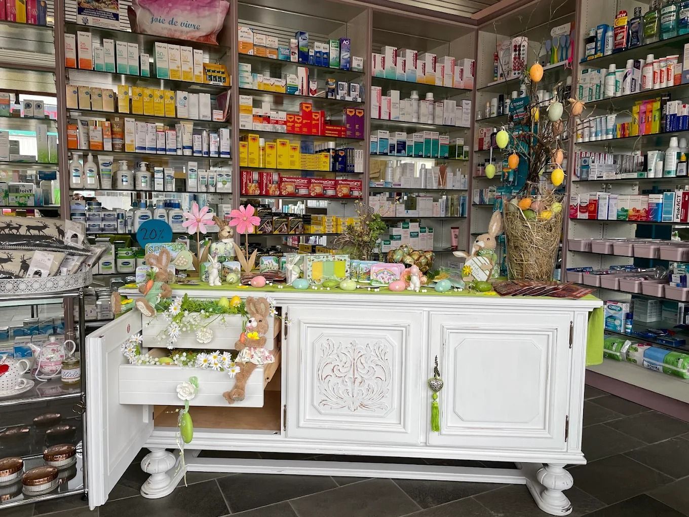 Interno colorato di un negozio di artigianato e articoli da regalo, con scaffali pieni di materiali e un tavolo espositivo decorativo bianco.