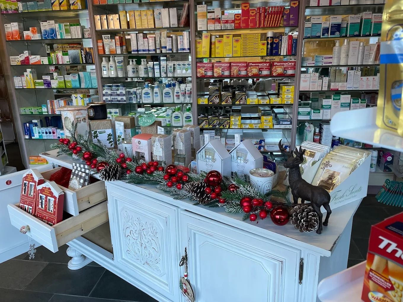 Bancone del negozio con scaffali pieni di articoli assortiti, decorato con ghirlande e ornamenti rossi.
