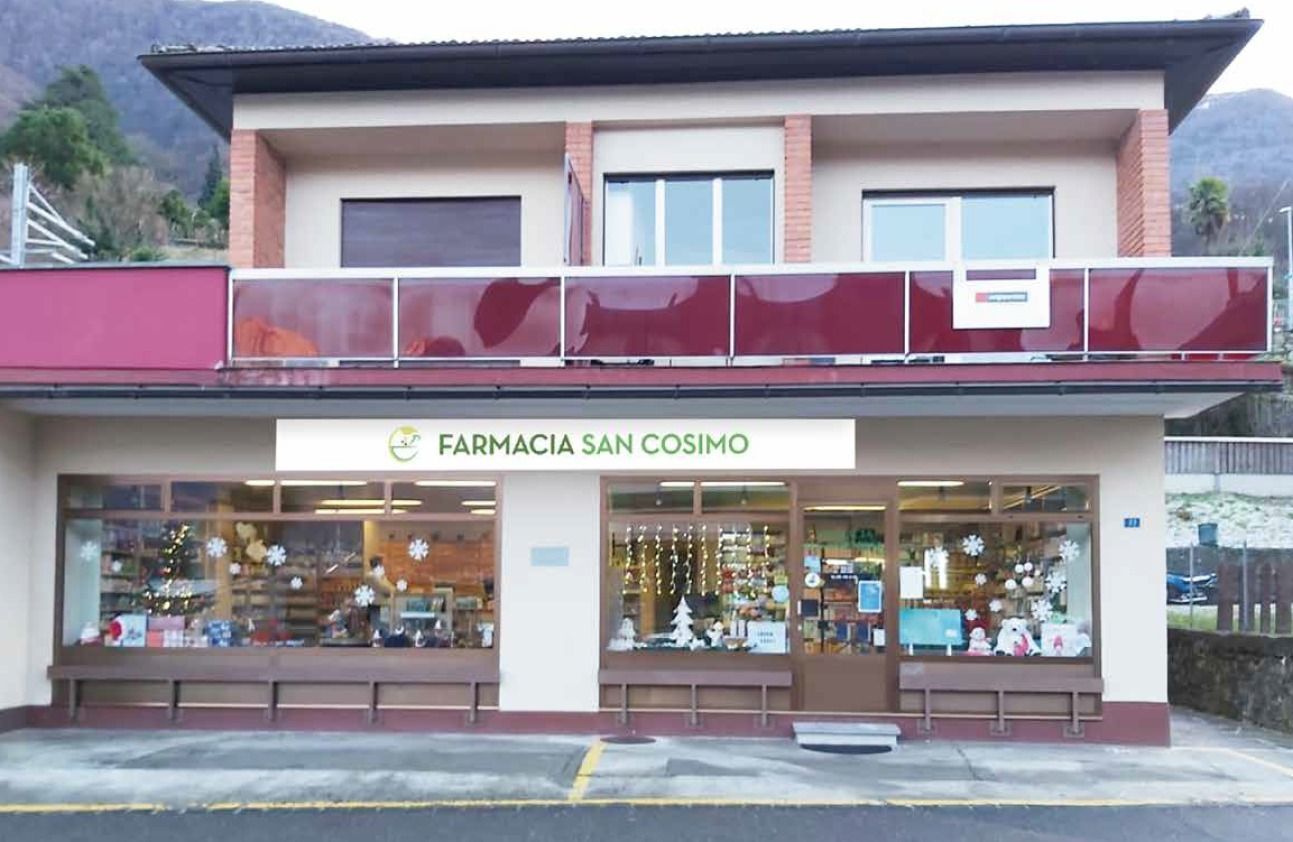 Esterno della Farmacia San Cosimo, una farmacia a due piani rosa e beige con vetrina e insegne.