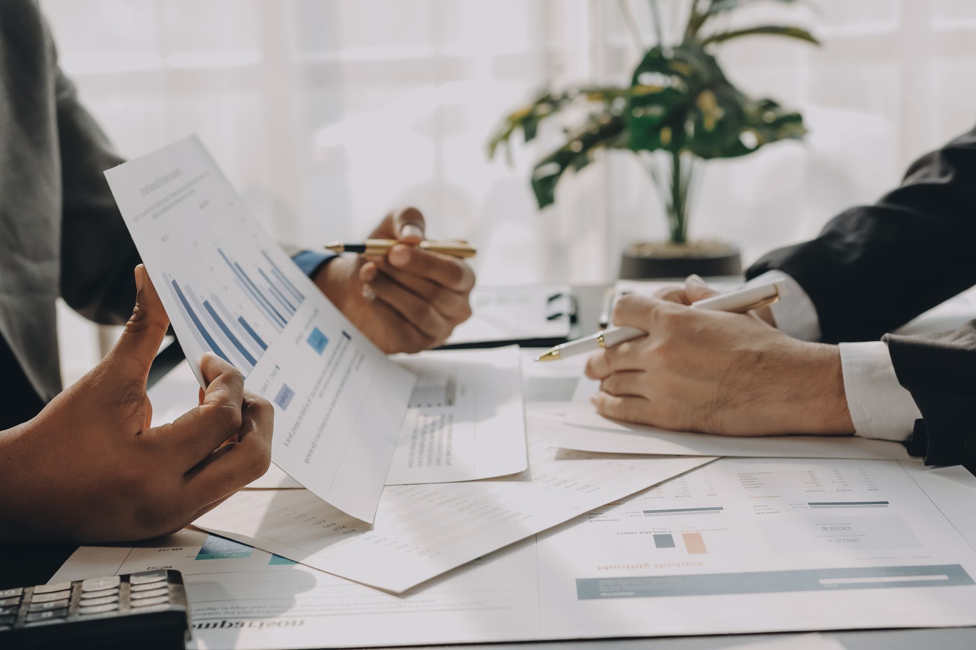 Dos personas de traje revisando documentos financieros con gráficos en un escritorio.