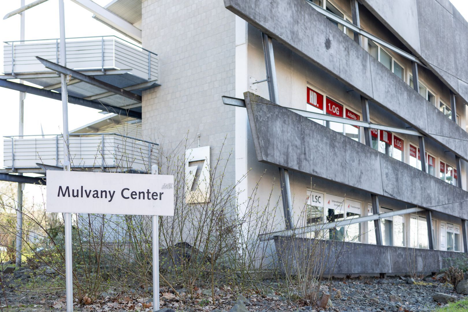 Ein Schild des Mulvany Centers steht neben einem grauen Wohnhaus mit Balkonen und vernagelten Fenstern.
