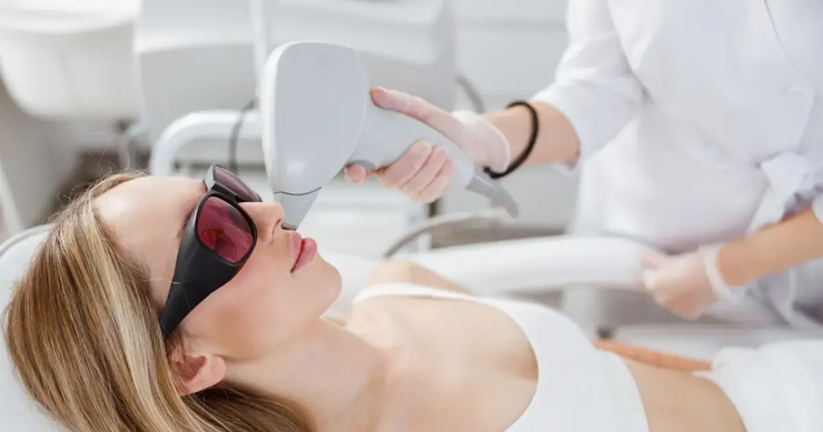 Mujer recibiendo tratamiento láser en el rostro, con gafas protectoras en un entorno médico.