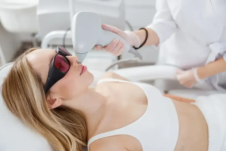 Mujer recibiendo tratamiento láser en el rostro, con gafas protectoras en un entorno médico.