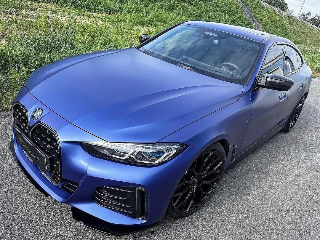 Sininen BMW-sedan pysäköitynä tielle vihreyden viereen, katsottuna vasemmalta edestä