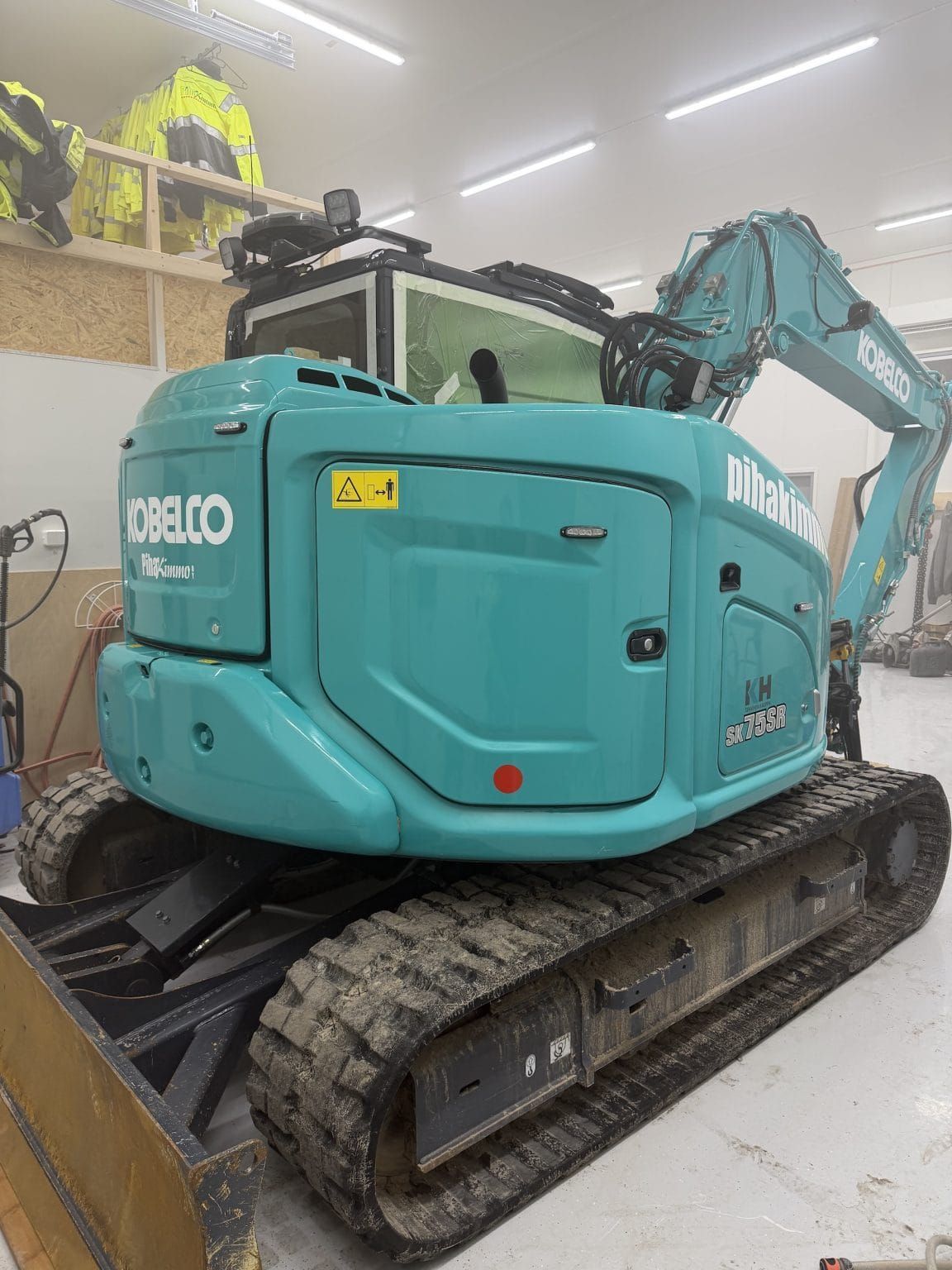 Turkoosi Kobelco-minikaivuri kiskoilla autotallissa, jossa on valkoinen betonilattia.