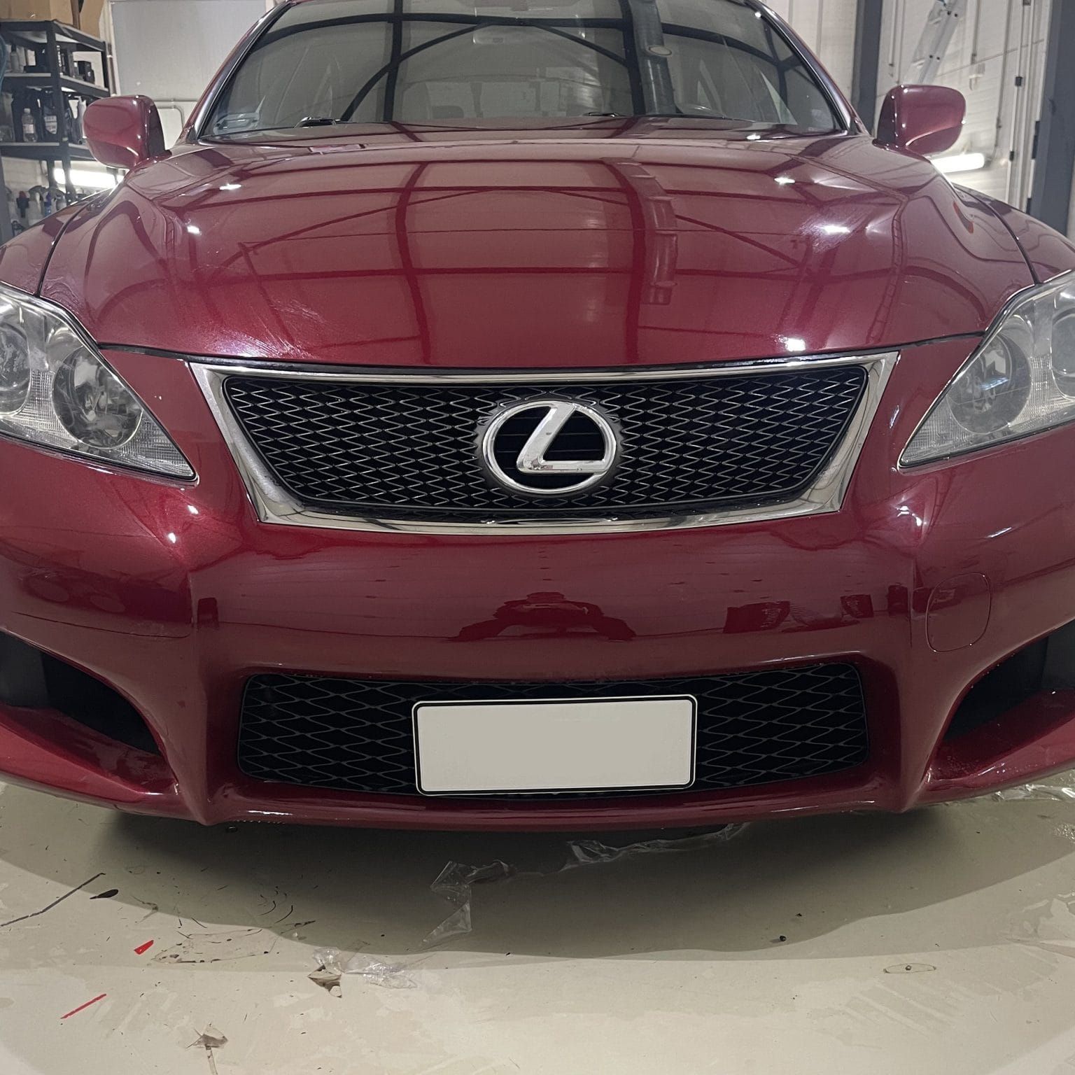 Edestä päin kastanjanruskea Lexus-sedan pysäköitynä autotalliin, jossa on sumea rekisterikilpi.