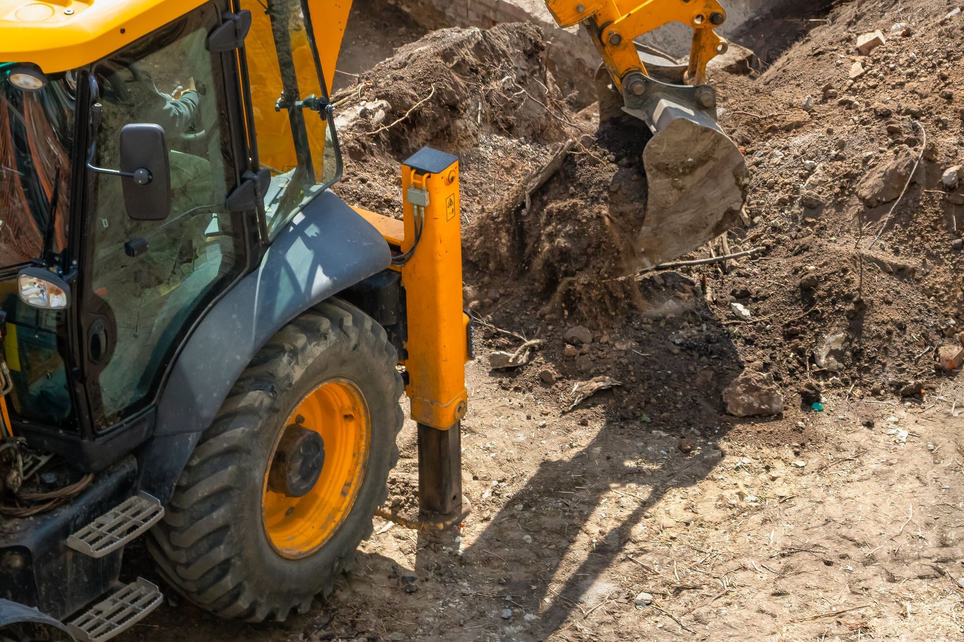 Une pelleteuse jaune utilise un marteau-piqueur pour briser la terre sur un chantier de construction.