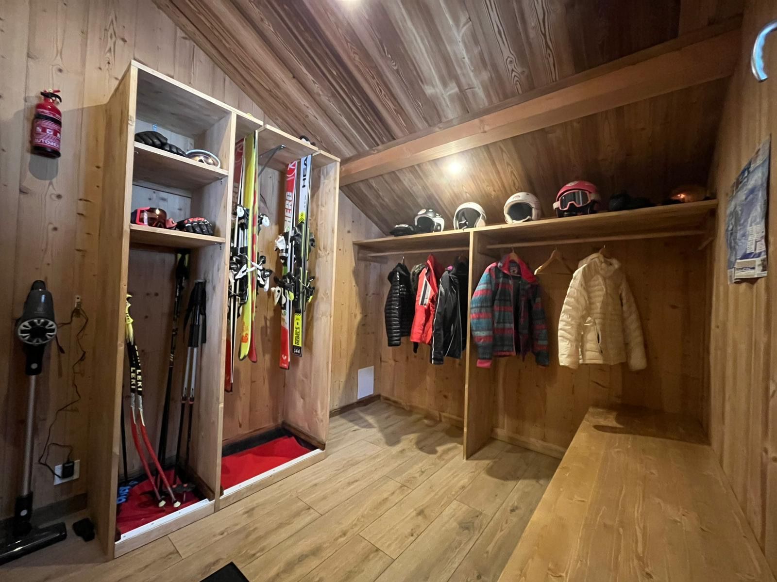 Un local à skis aux murs en bois, équipé de supports pour les skis, les bâtons, les casques et de portemanteaux.