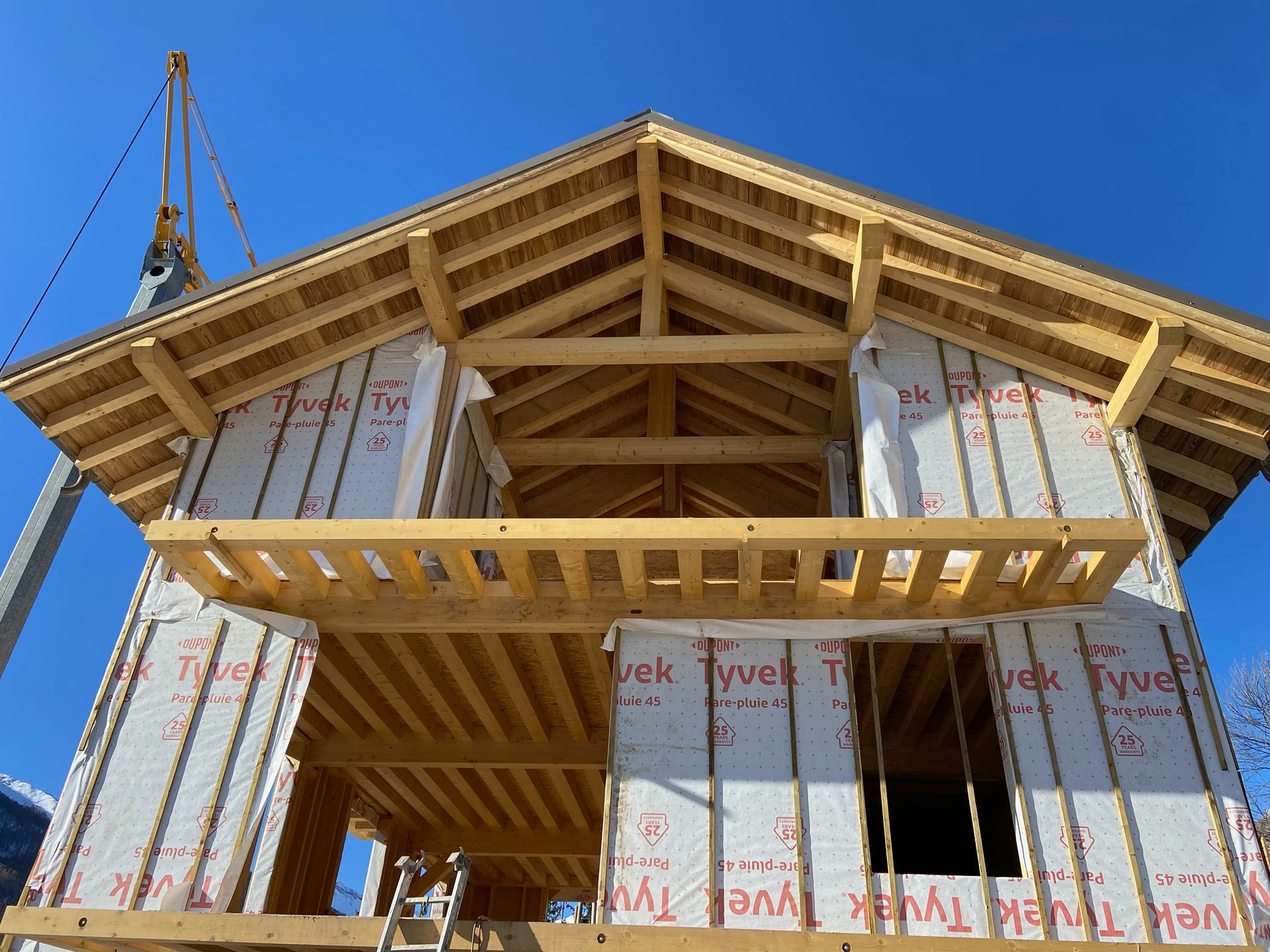 Une grande grue jaune se dresse à côté d'une maison à ossature bois en construction.