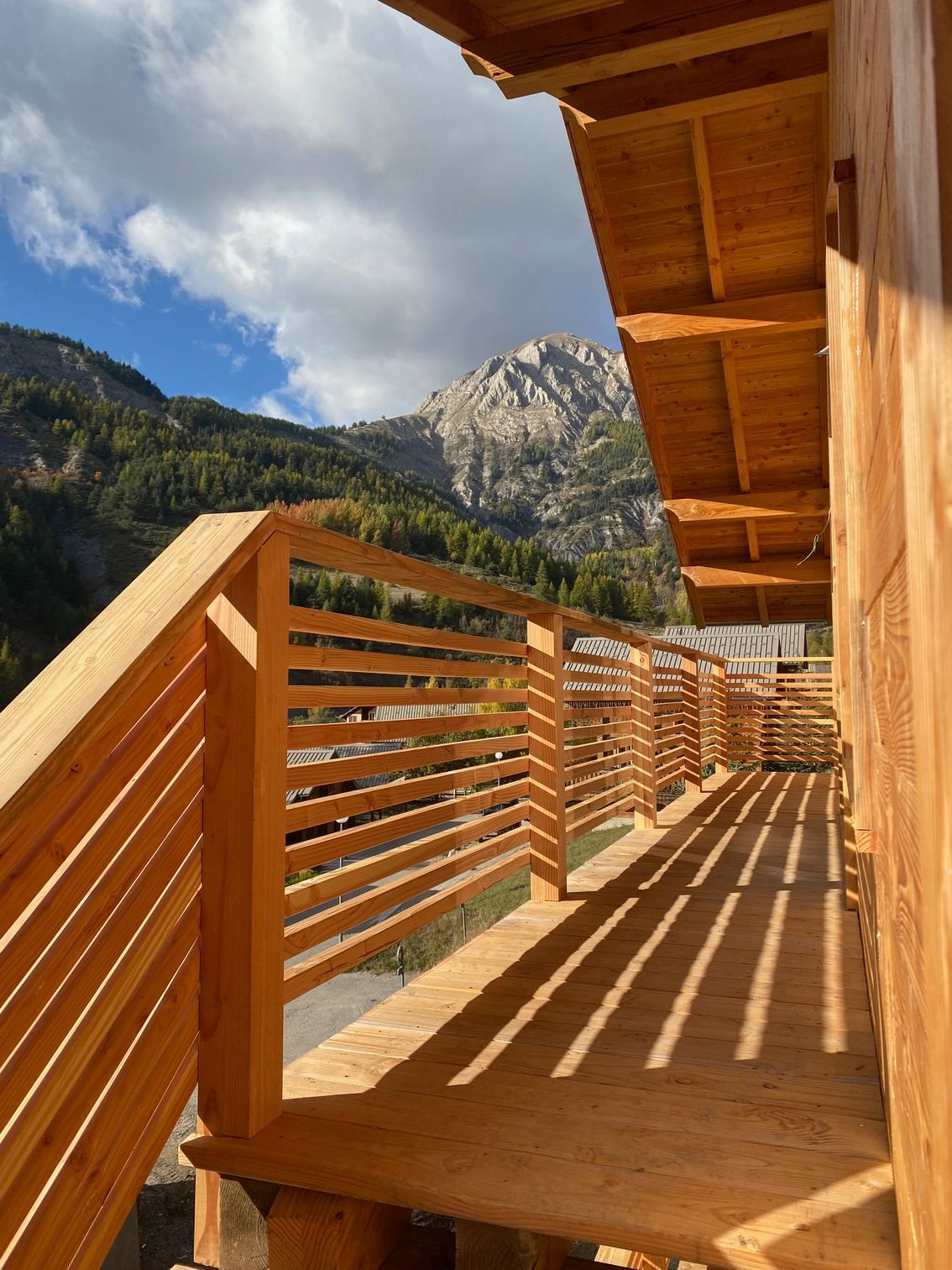 Un balcon en bois aux balustrades horizontales surplombe une vallée et une grande montagne escarpée.