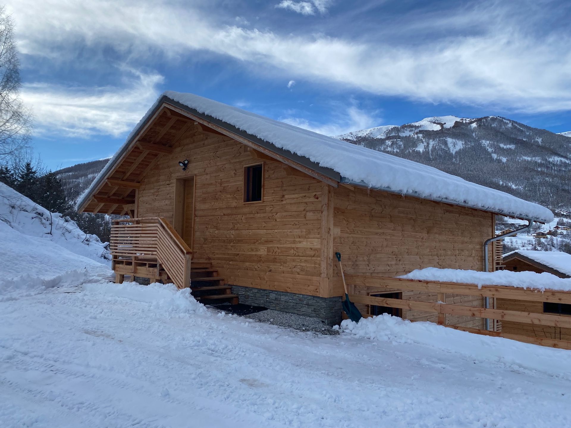 Un chalet en bois au toit enneigé, nichée dans un paysage montagneux enneigé sous un ciel d'un bleu éclatant.