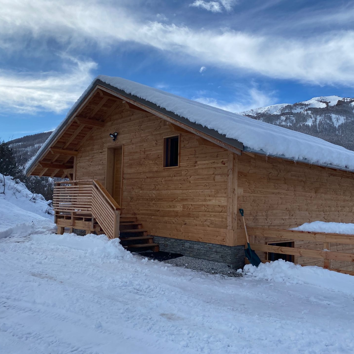 Un chalet de montagne en bois, entouré de neige, sous un ciel d'un bleu éclatant parsemé de quelques nuages ​​légers.