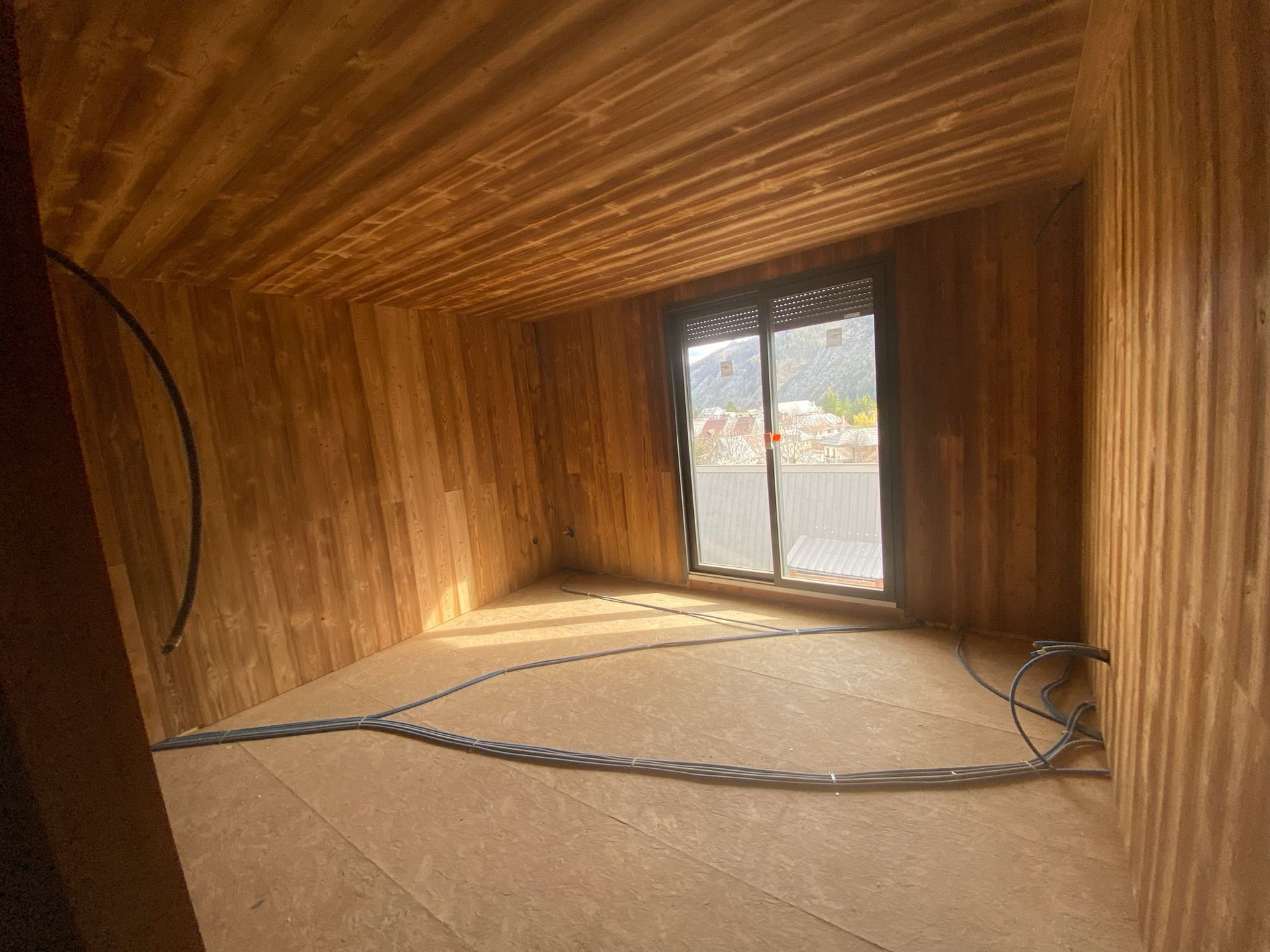 Une pièce en construction avec des murs lambrissés et une porte coulissante en verre.