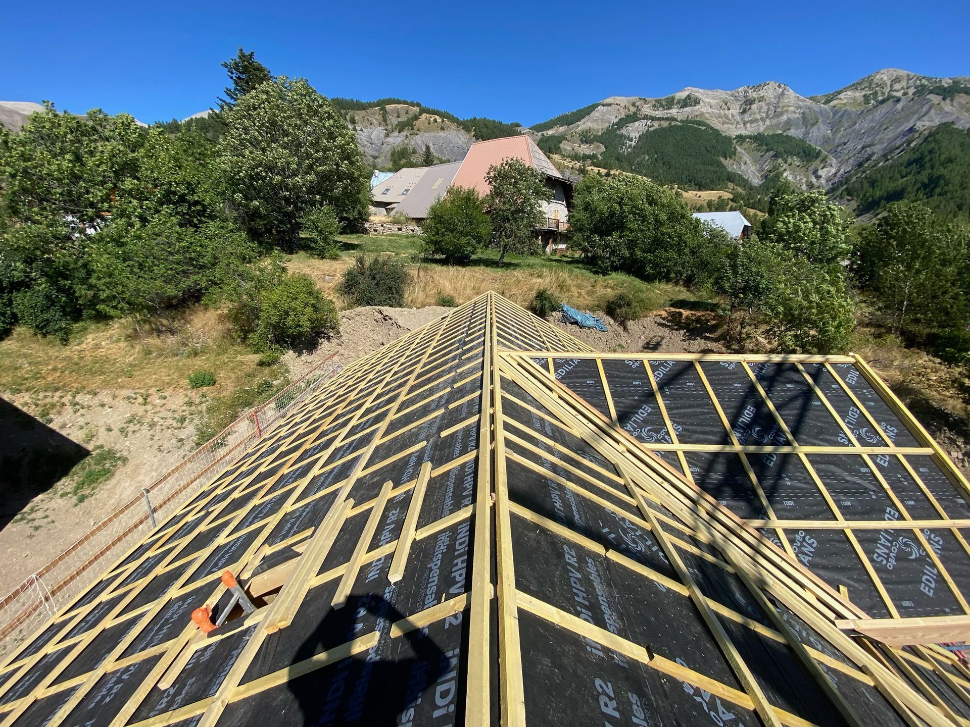 Une charpente de toit en bois avec une sous-couche noire est en cours de construction.