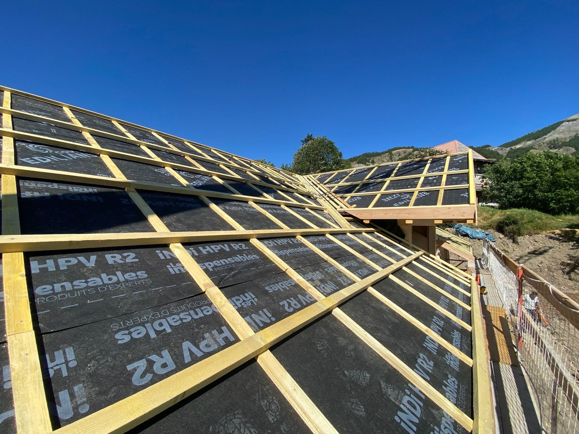 Des travaux de charpente avec des liteaux en bois installés sur une membrane d'étanchéité noire.