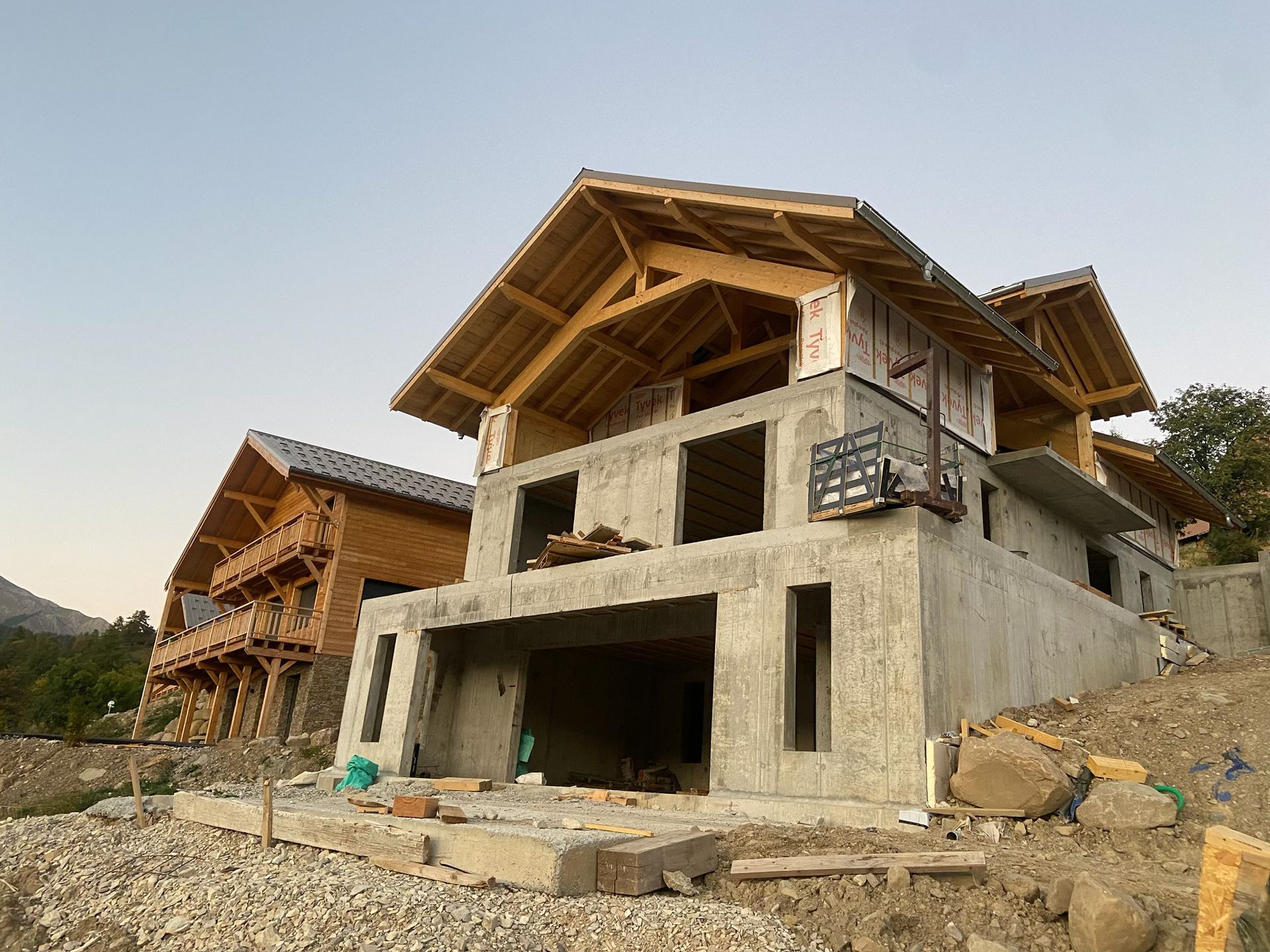 Un engin de chantier est stationné devant une structure en bois partiellement construite.