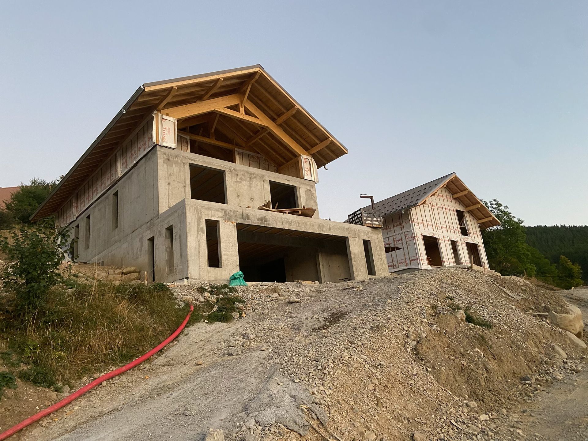 Chantier de construction avec une structure en bois partiellement édifiée et un chariot télescopique vert garé devant.