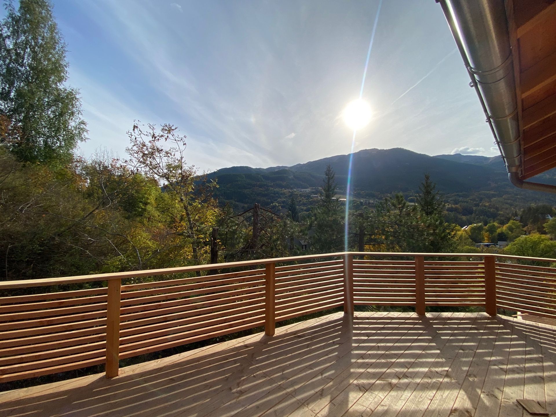 Terrasse en bois ensoleillée avec rambarde donnant sur un paysage montagneux
