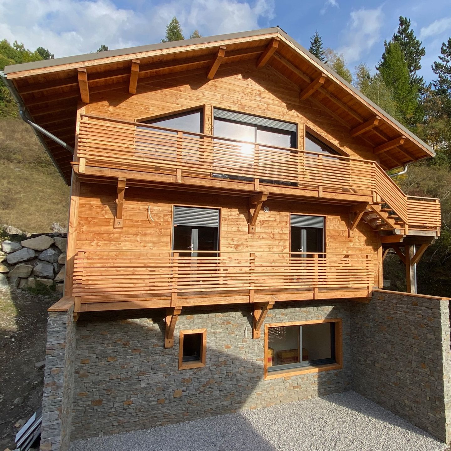 Un chalet en bois à plusieurs étages en construction, avec des fondations en pierre et des balcons.