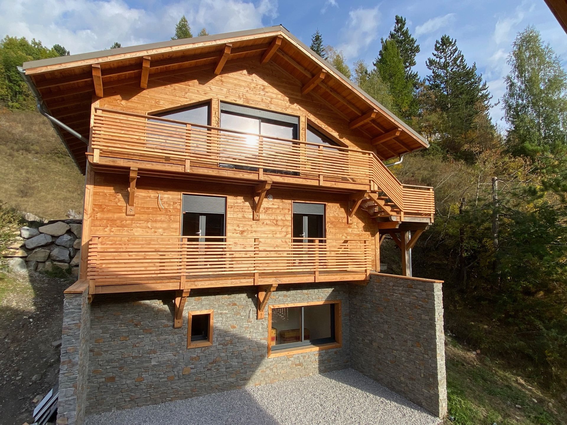 Maison de style chalet en bois avec fondations en pierre sur un flanc de colline