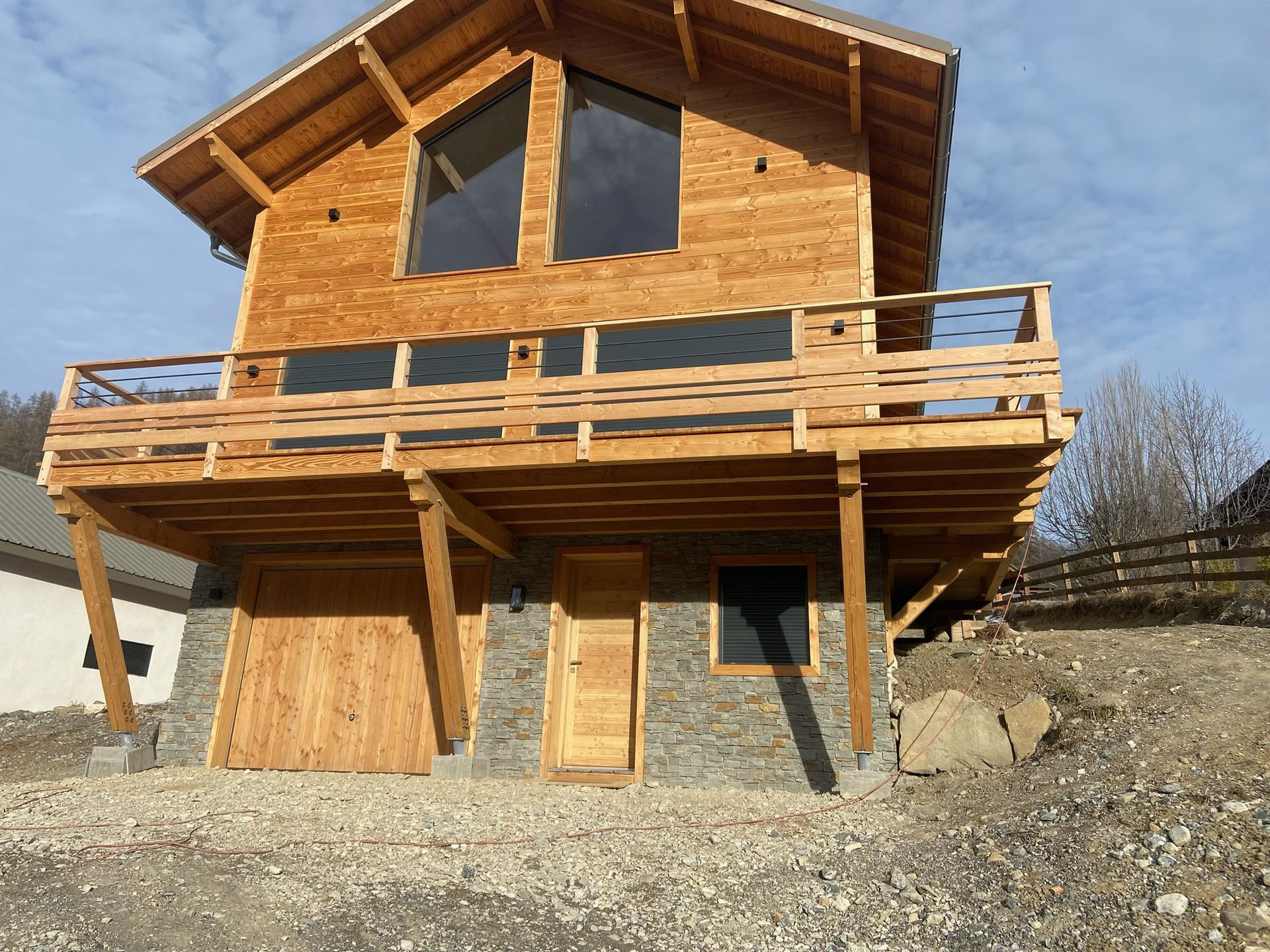 Chalet en bois avec balcon et grandes fenêtres sur une pente de gravier