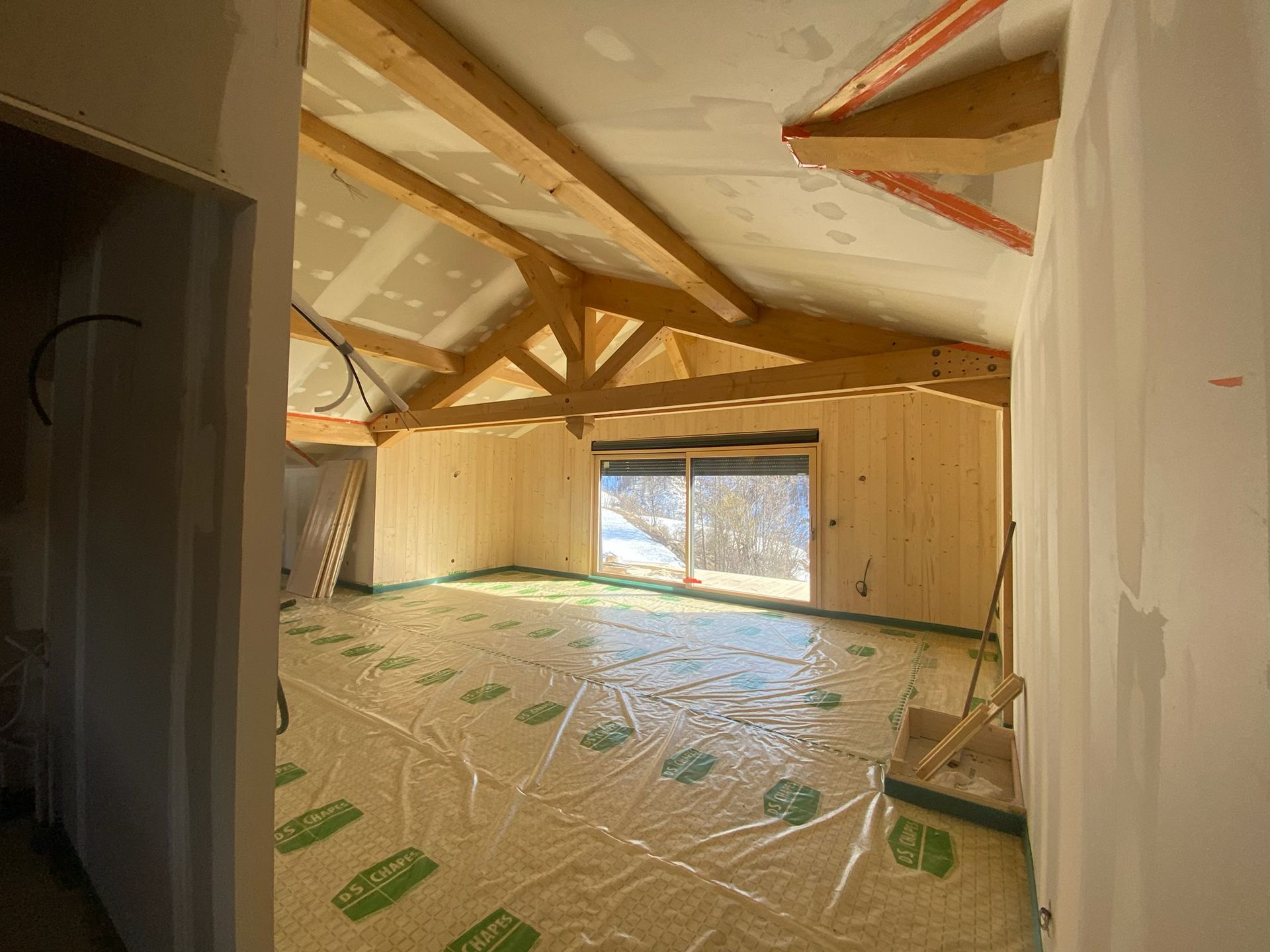 Chalet rénové avec ossature bois apparente, murs lambrissés et sol recouvert de plastique en cours de construction
