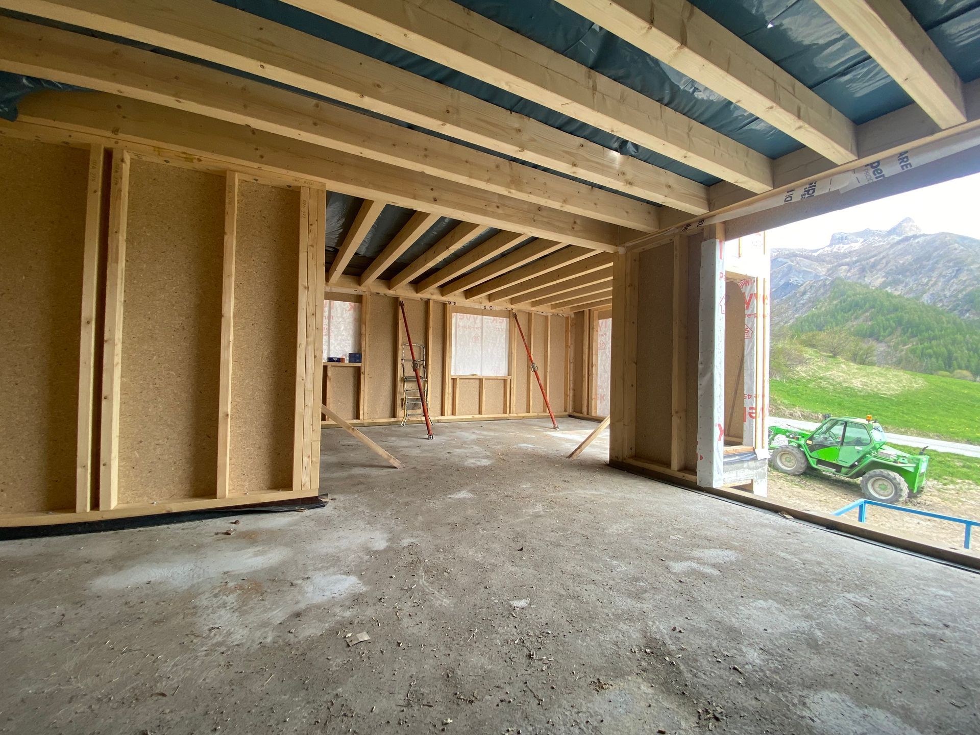 Vue intérieure d'un bâtiment en construction avec charpente et plafonds en bois apparents.