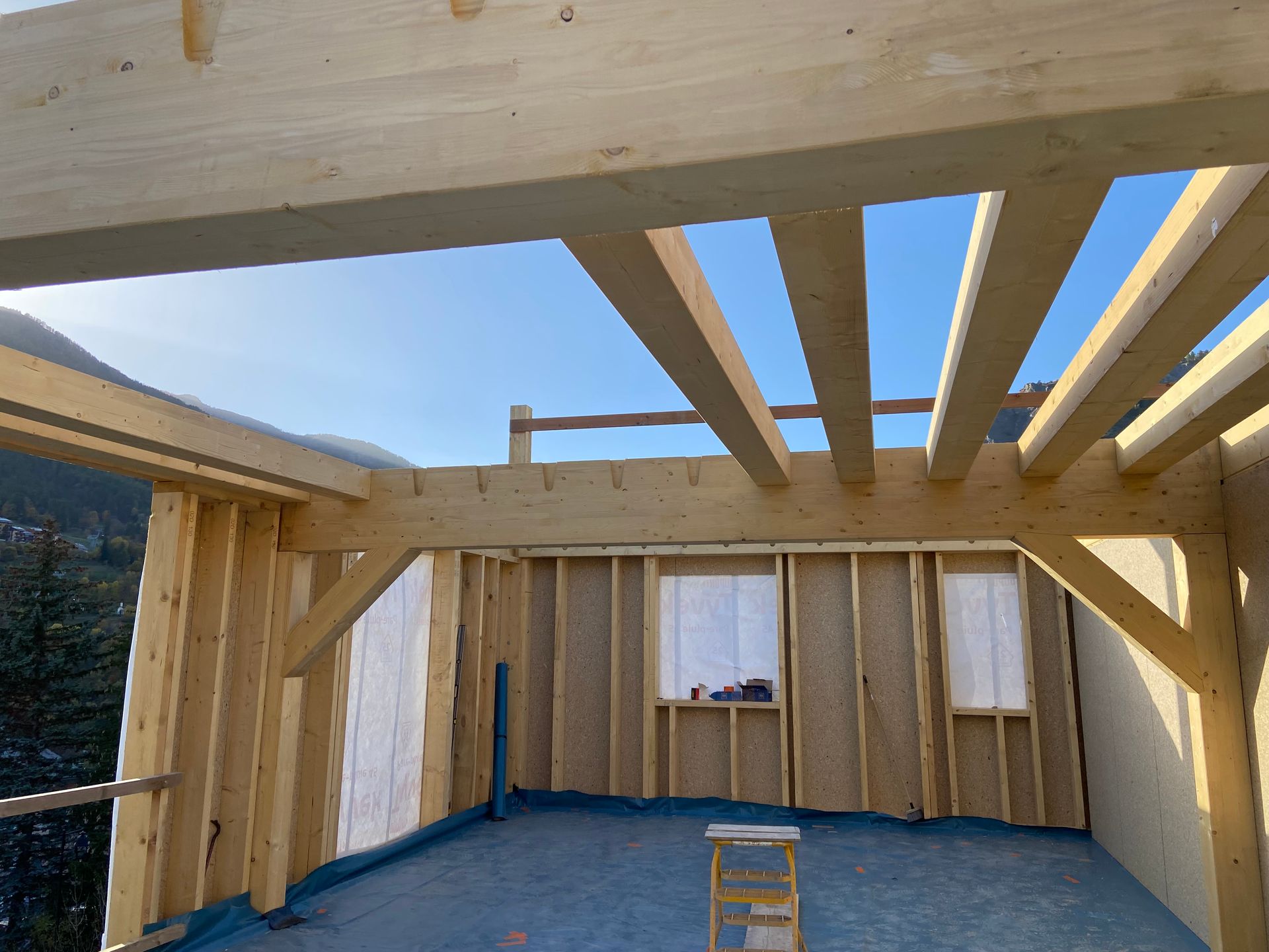 Charpente en bois inachevée d'un intérieur de bâtiment, avec solives de plafond apparentes.