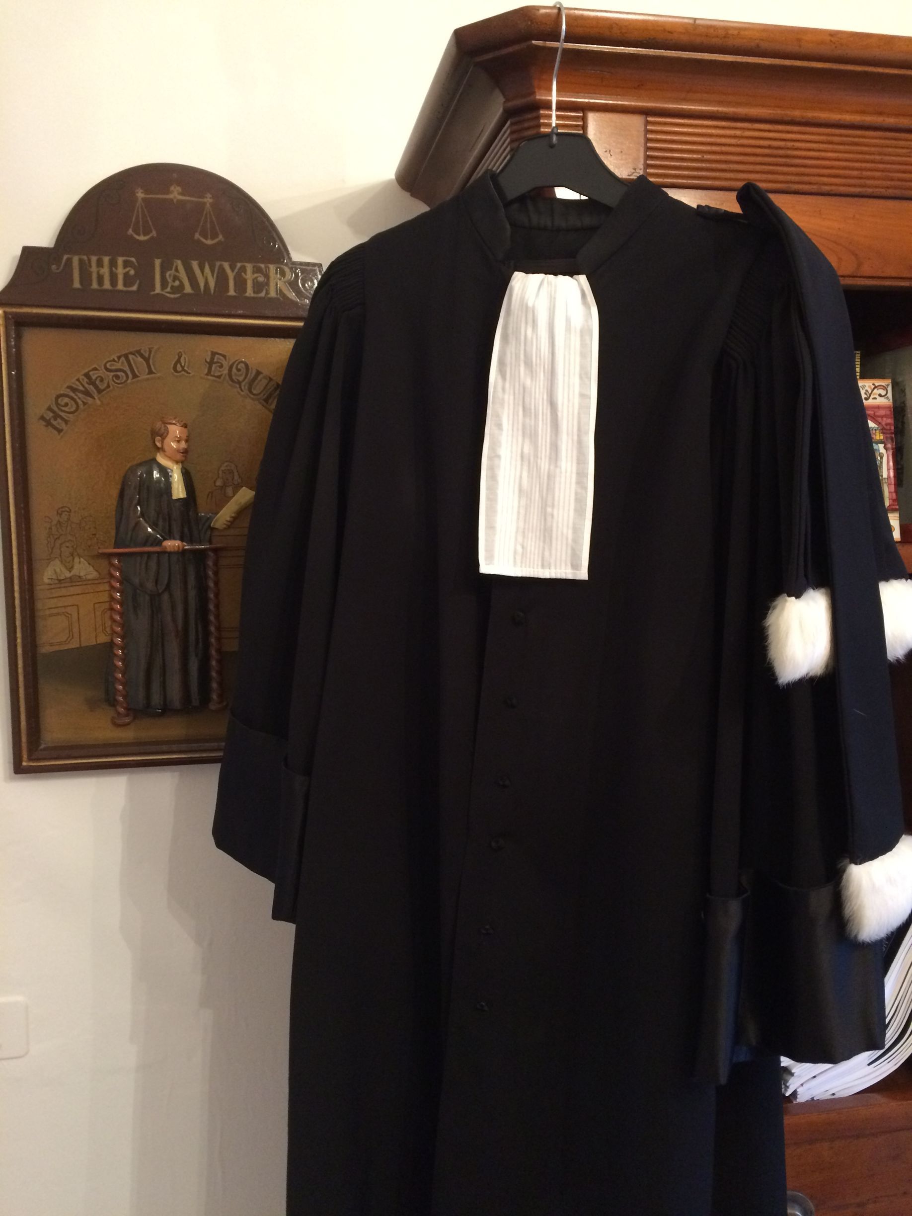 Robe d'avocat noire à pattes blanches, accrochée à l'intérieur à côté d'une plaque.