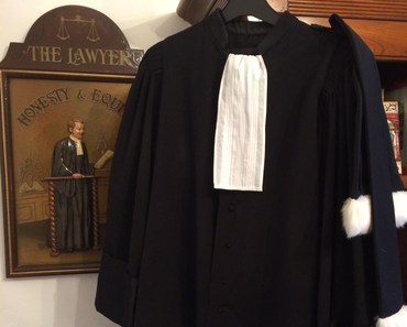 Robe d'avocat noire avec pattes de col blanches, suspendue dans un bureau d'avocat ou une salle d'audience.
