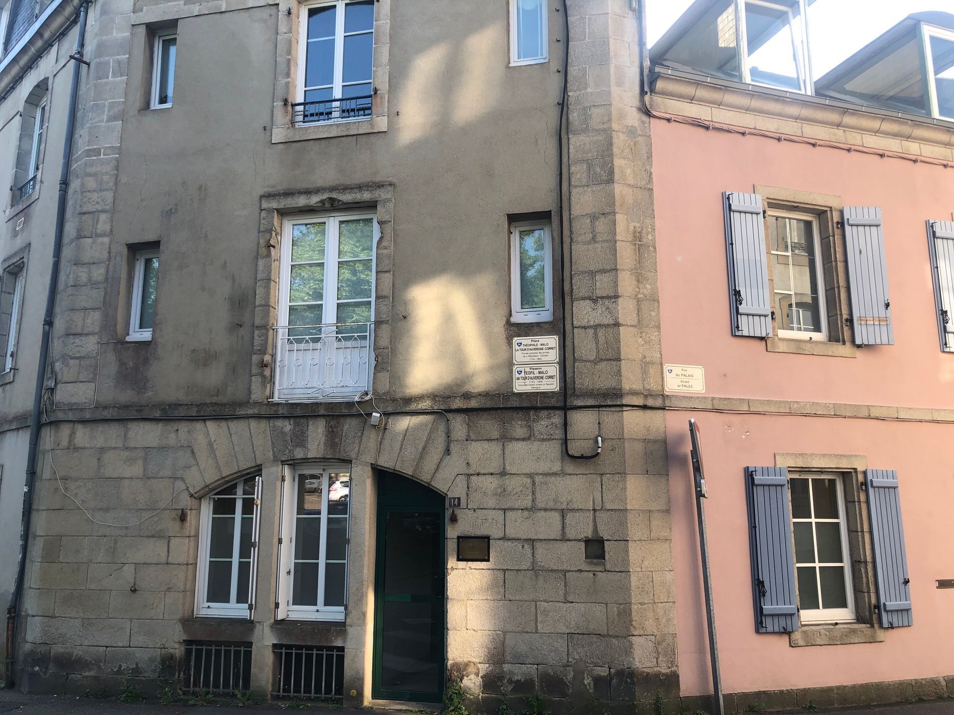De vieux immeubles en pierre rose aux fenêtres à volets bordent une rue étroite.