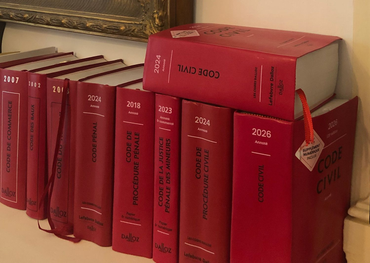 Des livres à couverture rigide rouge alignés sur une étagère, beaucoup avec des étiquettes blanches et des marque-pages en ruban rouge.