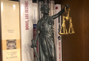Statue de la Justice en bronze tenant une balance sur une étagère à côté de livres aux titres français.