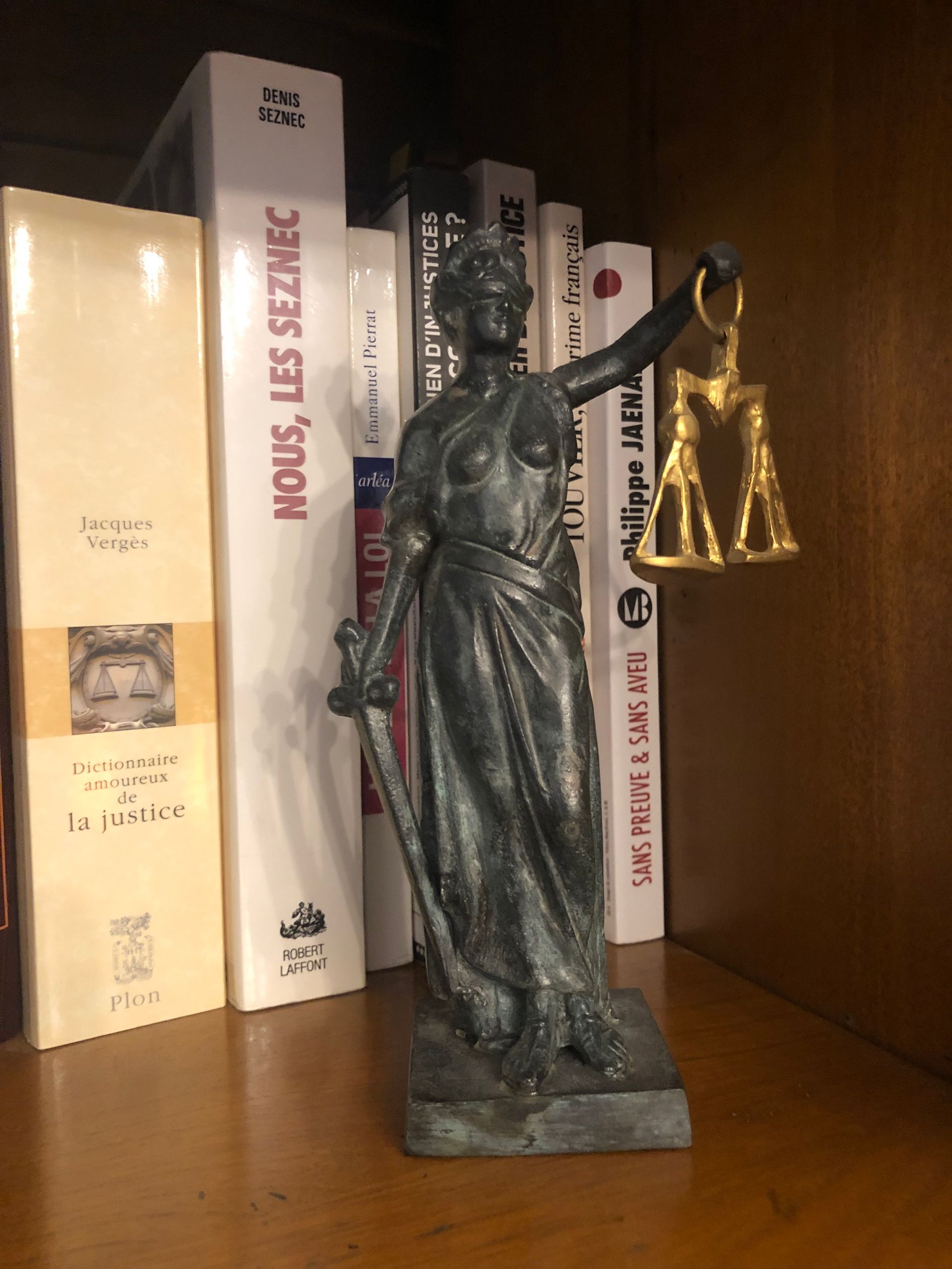 Statue en bronze sur une étagère, devant plusieurs livres et une petite figurine en or.