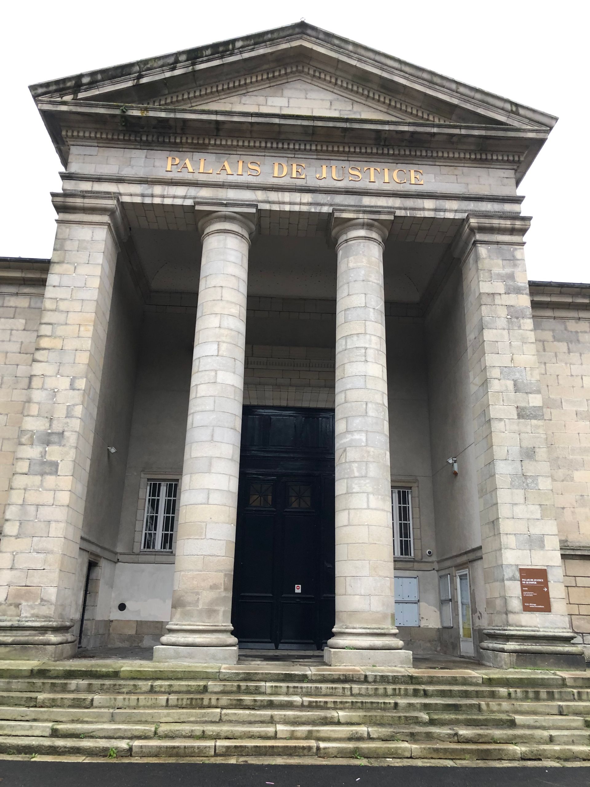 Bâtiment néoclassique en pierre avec deux grandes colonnes et des marches menant à une entrée sombre.