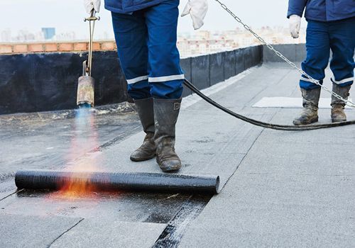 Dos hombres están trabajando en un tejado con una antorcha.