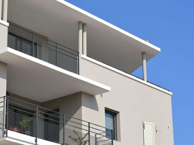 Immeuble d'appartements moderne beige avec balcons à plusieurs niveaux dotés de garde-corps en métal noir se détachant sur un ciel bleu clair.