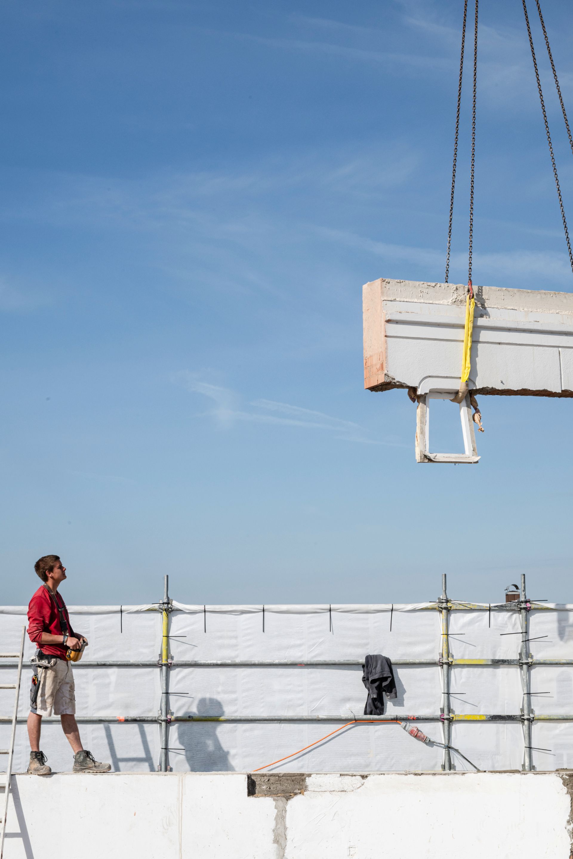 Arbeiter überwacht Einheben eines Betonelements auf dem Dach eines Rohbaus
