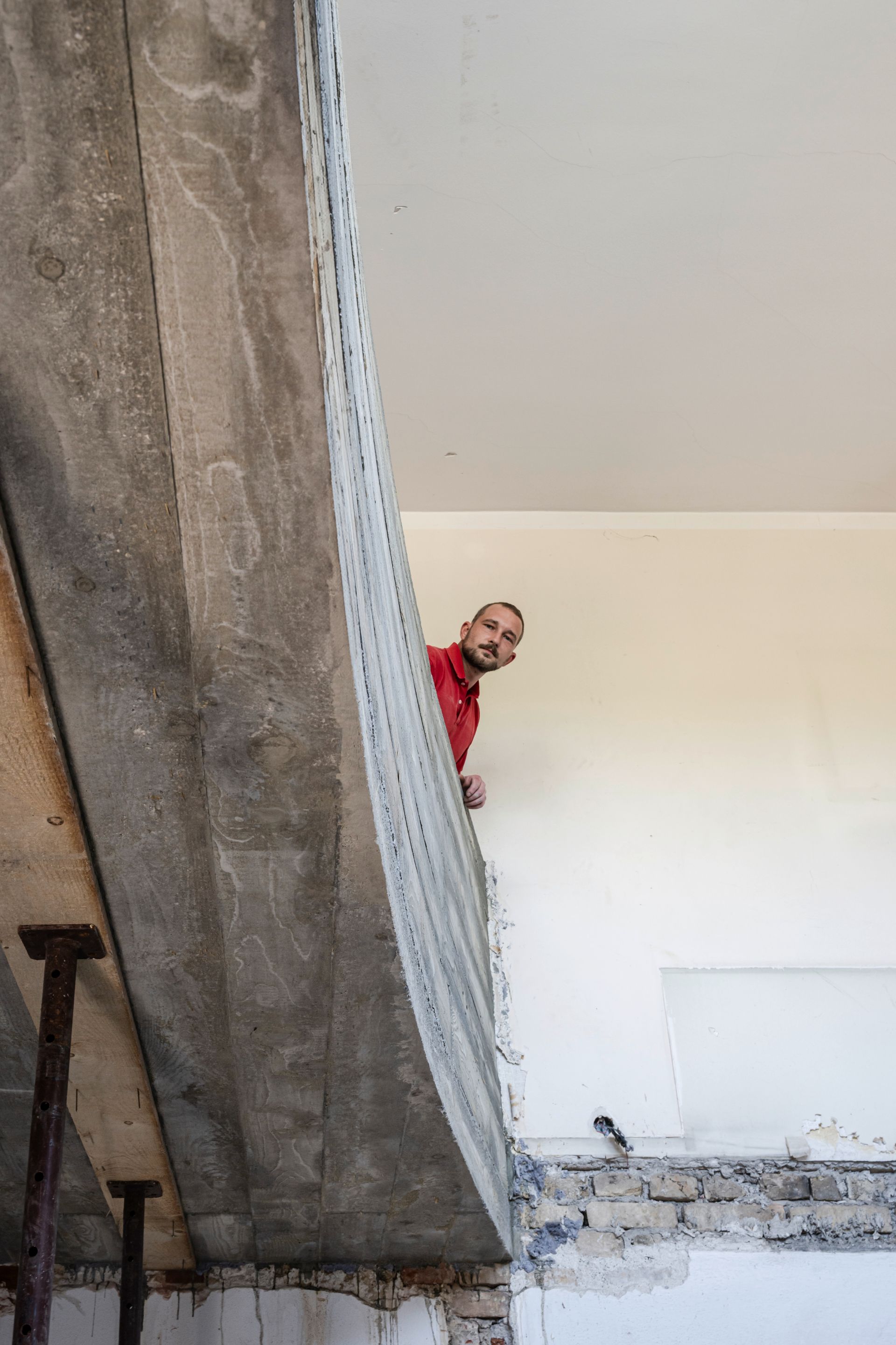 Handwerker schaut hinter Betonstütze hervor auf Baustelle