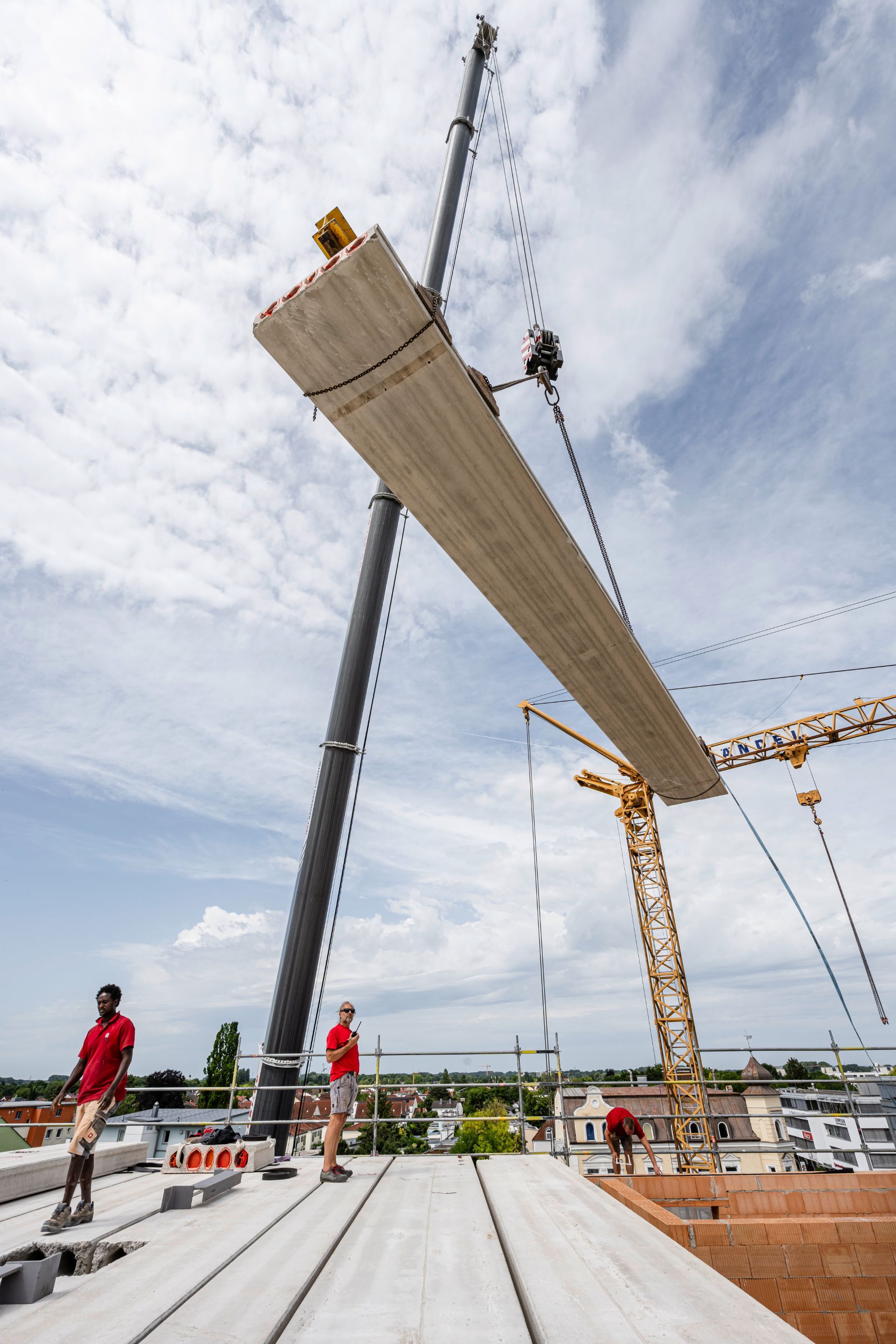 Betonträger wird per Kran auf Rohbaufläche abgesenkt